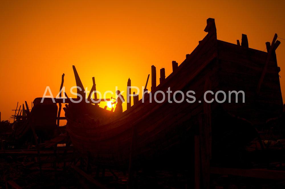 In the last light of Twilight, a craftsmen passing busy time in making on wooden boat at Noakhali, Bangladesh. According to the boat makers, the dry season, especially from December to June, is the ideal time for making the fishing boats. Craftsmen are hammering the nail in the wooden body of the ship and they are working till the end because the ships will have to float in the sea shortly after them.